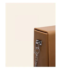 Close-up of silver metal hardware hook and ring on a tan leather mini crossbody bag