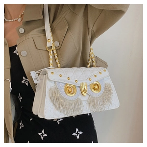 Close-up of white quilted owl handbag featuring gold hardware and beaded tassels