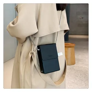 Detail of a minimalist black leather chain bag worn over a beige trench coat for women
