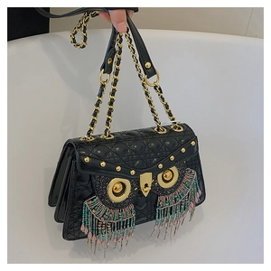 Macro view of black quilted crossbody bag with golden owl eyes and colorful tassels