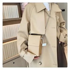 Chic beige mini crossbody bag with a slim metal chain shown against a book backdrop