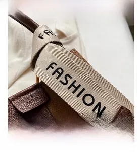Detail of brown leather bucket bag featuring a wide woven strap with FASHION text