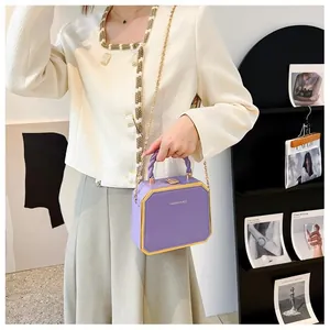 Detail of purple hard shell box bag featuring gold trim and elegant chain strap