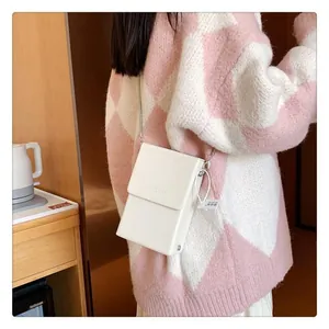 Minimalist white leather phone bag with silver chain worn over a checkered sweater