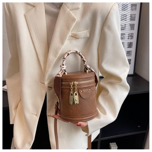 Détail d'un sac seau cylindrique marron avec poignée enroulée d'un foulard et double fermeture