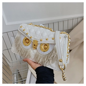 Detail of white quilted crossbody bag with golden owl eyes hardware and fringe accents
