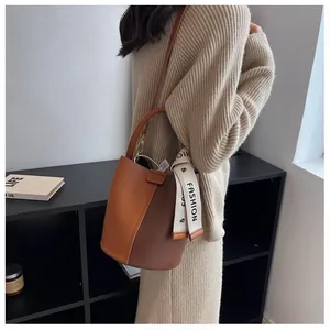 Detail of color-block bucket bag with litchi grain texture and fashion ribbon strap
