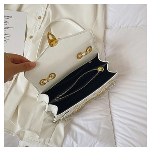 Detail of white leather crossbody bag with gold buckle and silver fringe tassels