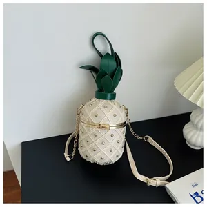 Détail du sac seau ananas avec clous dorés et feuilles vertes posé sur une table
