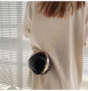Chic black spherical acrylic evening bag with gold chain strap shown on a model's shoulder