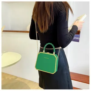 Detail showing green hard-shell box bag with gold metal trim and woven handle texture