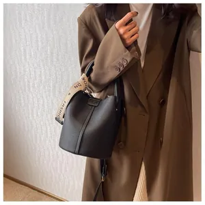 Detail of black pebbled leather bucket bag with decorative scarf on handle and shoulder strap