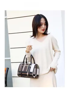 Classic checkered Boston handbag with leather handles worn over the shoulder by a model