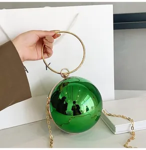 Macro detail of a spherical green mirror-finish mini bag with golden metal ring handle