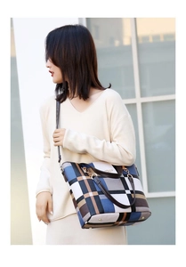 Detail of vintage plaid shoulder bag with brown leather handles and golden metal hooks