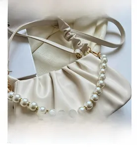 Detail view of white ruched cloud bag featuring large pearl strap and soft pleated texture