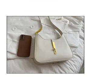 Detailed top view of a white shoulder bag with gold hardware next to a phone for size