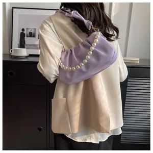 Detail of lavender pleated cloud bag with pearl chain strap on shoulder of a model