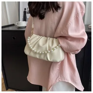 Close-up of cream pleated cloud bag with large pearl chain on model's shoulder