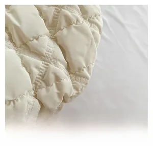 Detailed close-up of cream quilted puffer fabric with soft padding and rhombus texture