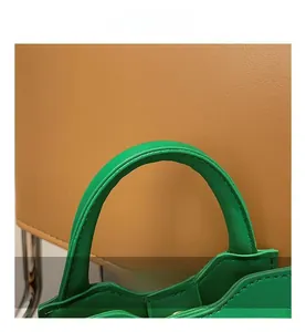 Detail of contrasting green litchi grain leather handle on brown woven handbag