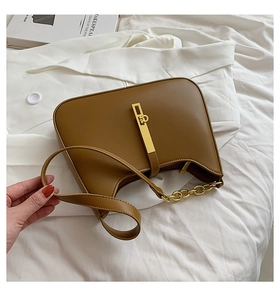 Close-up of caramel brown shoulder bag with golden metal buckle and chain on white linens