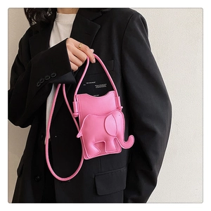 Détail du sac bandoulière rose en forme d'éléphant porté sur un blazer noir