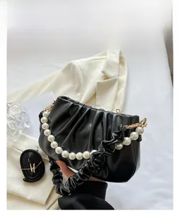 Detail of black pleated cloud bag featuring large pearl handle and gold hardware accents