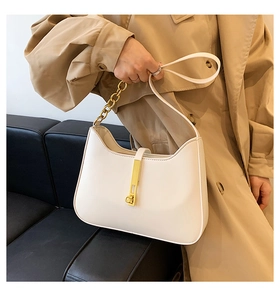 Detail of white leather crescent bag with golden chain and metallic buckle on black sofa