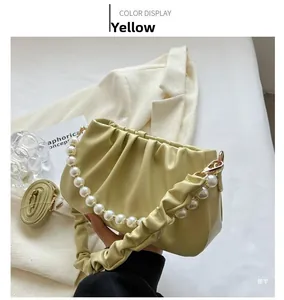 Detail of soft pleated cloud bag in pale yellow featuring a large white pearl handle