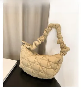 Close-up of khaki quilted puffy shoulder bag with ruched strap on a display surface