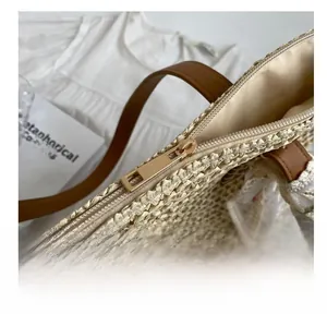Detail of the smooth gold zipper and brown leather handle on a beige woven tote bag