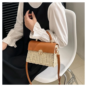Detail view of a woven straw crossbody bag with brown leather flap and gold metal clasp