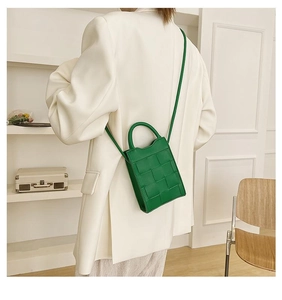 Green woven leather small square bag carried over the shoulder of a white suit jacket