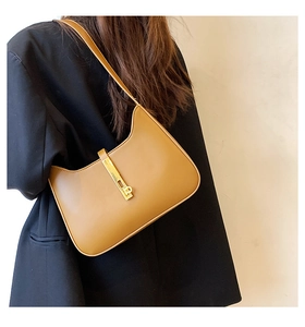 Detail of a brown leather shoulder bag with a gold metal clasp worn by a model in black
