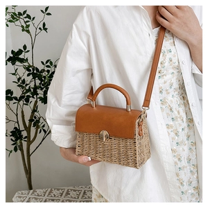 Detail of woven straw handbag with brown leather flap and golden twist lock closure