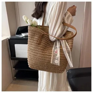 Detail of hand-woven straw tote bag with brown leather straps and lace scarf charm