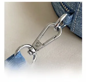 Close-up of polished silver lobster clasp and blue denim strap with white stitching