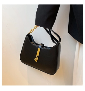 Detail of black faux leather underarm bag with gold metal vertical bar and chain strap