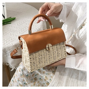 Detail of woven straw handbag featuring brown leather flap and golden twist lock