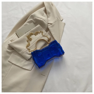 Détail du sac nœud en acrylique bleu avec poignée dorée sur blazer beige et tissu blanc
