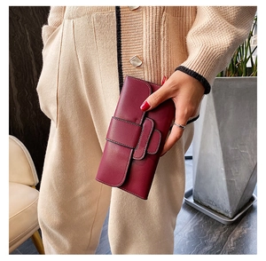 Close-up of a burgundy leather long wallet with a decorative metal buckle held by a model