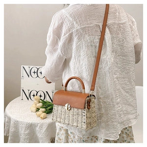 Detail of woven straw bag with brown leather flap and golden lock on a summer table