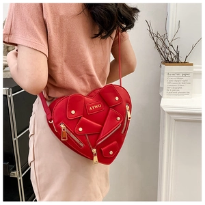 Detail of red heart-shaped biker style crossbody bag with zippers and studs worn by model