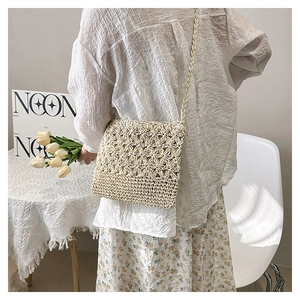 Détail de la texture en tricot ajouré fait main sur un sac bandoulière en paille crème