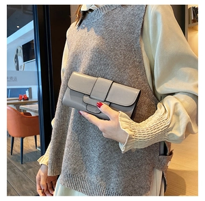 Detail view of a taupe leather long wallet with foldover flap and buckle clasp held by hand