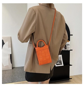 Detail of a bright orange woven mini crossbody bag with a modern top handle and slim strap