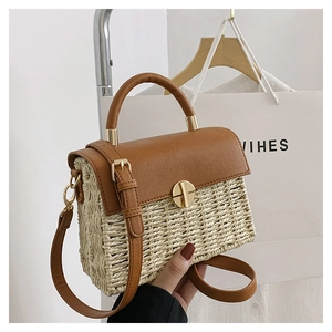 Detail of woven straw handbag featuring brown leather trim and a gold metal disc lock