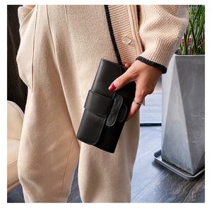 Detail of a minimalist black leather long wallet with a horizontal buckle held by a hand