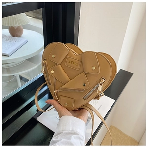 Detail of khaki heart-shaped crossbody bag featuring motorcycle jacket zippers and metal studs